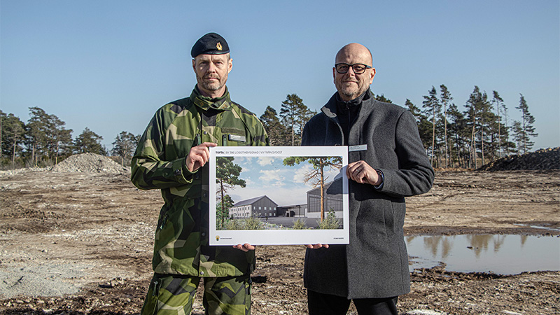 Två män håller tillsammans upp en bild med en illustration av en byggnad.