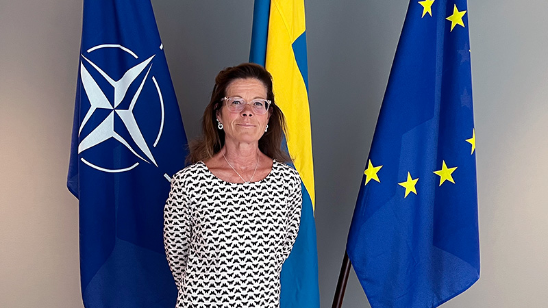 Fortifikationsverkets generaldirektör framför tre flaggor. Natoflagga, Sverigeflagga och EU-flagga.