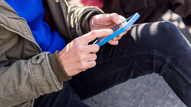 Person sitter med en mobil i handen. 