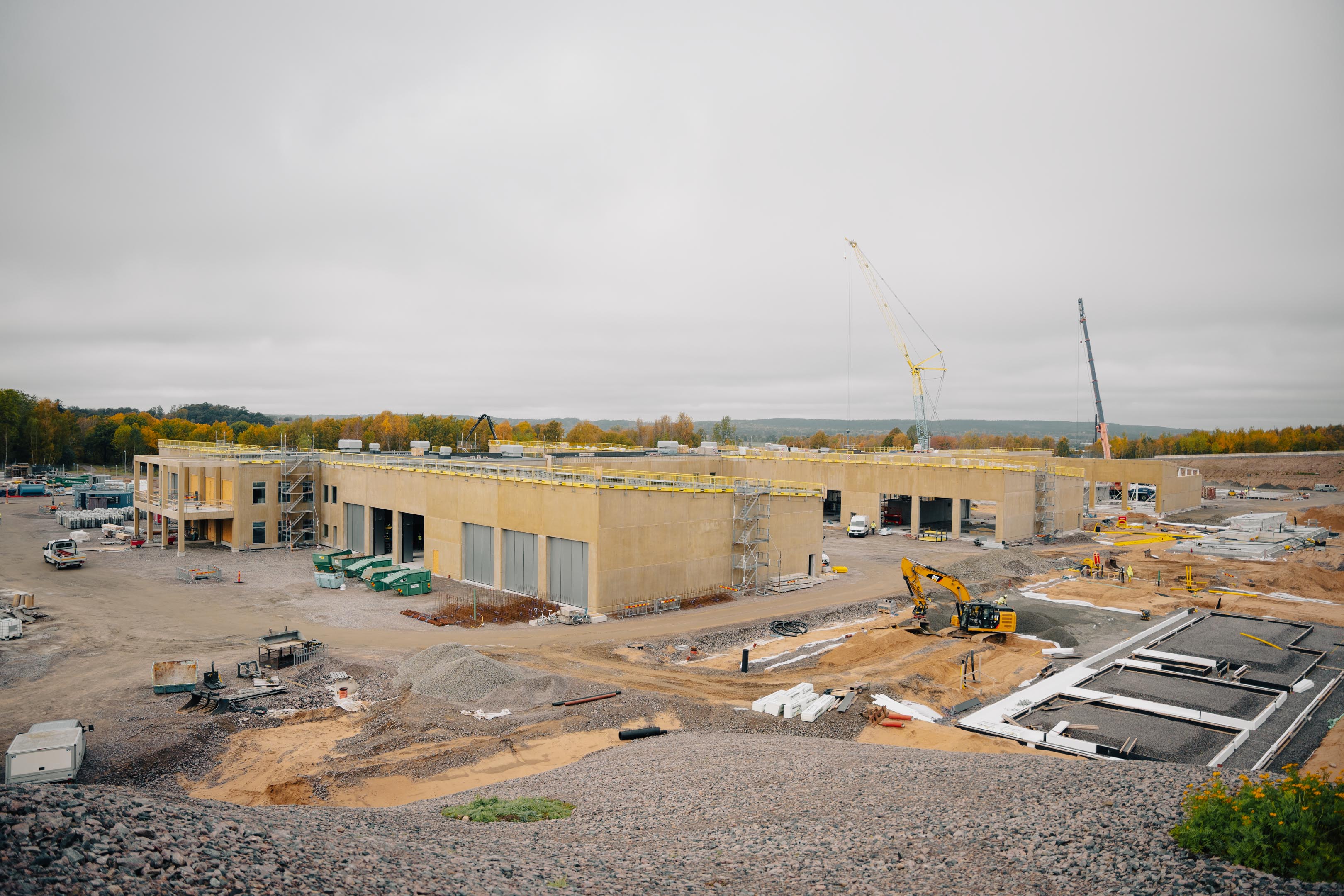 En pågående byggnation av en stor byggnad med kranar och grävsmaskiner runt omkring.