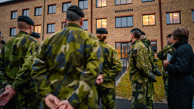 Ett antal personer i grön uniform står framför en tegelbyggnad